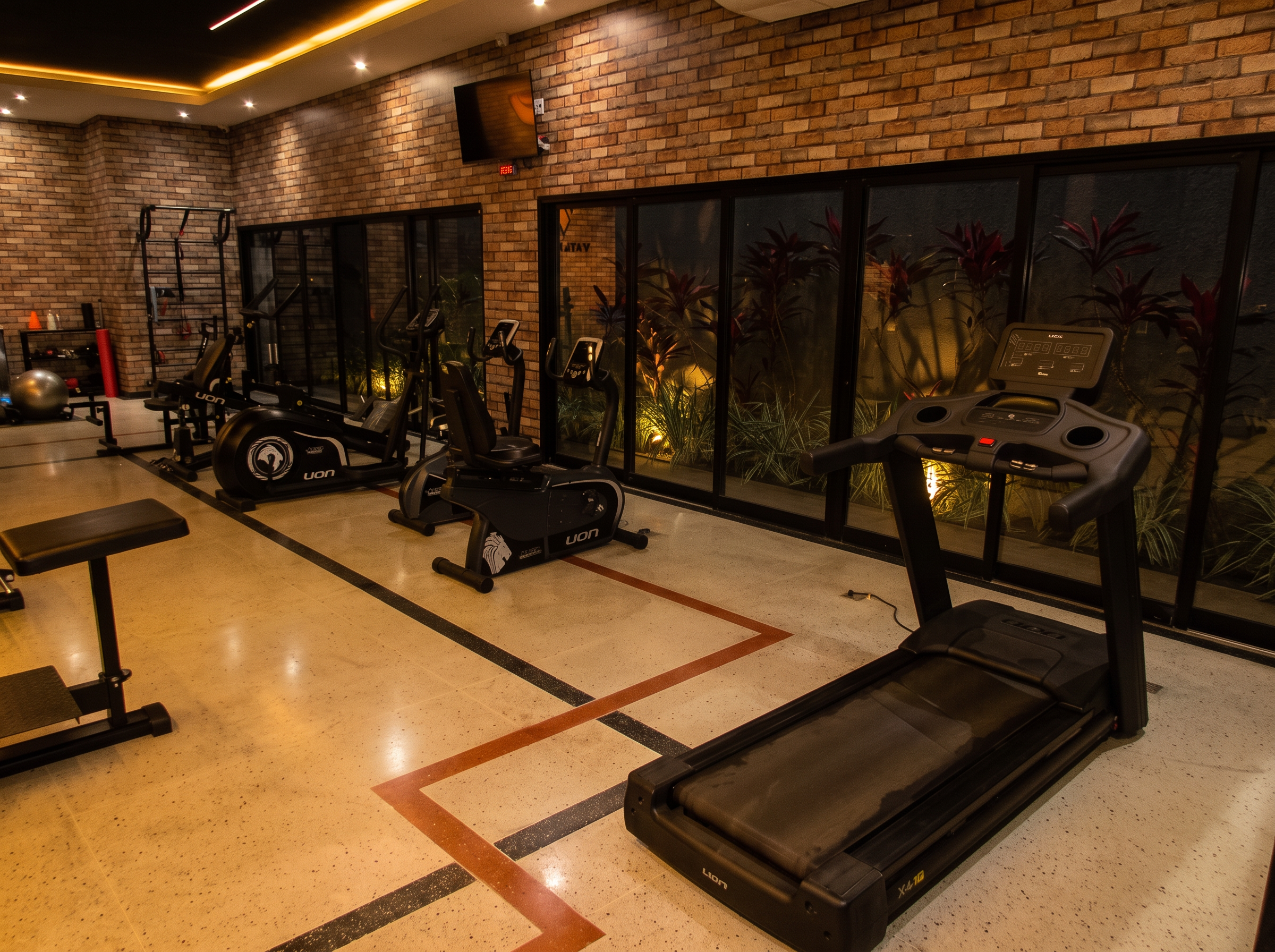 Área de cardio com esteira, bicicletas e elíptico com vista para o jardim iluminado