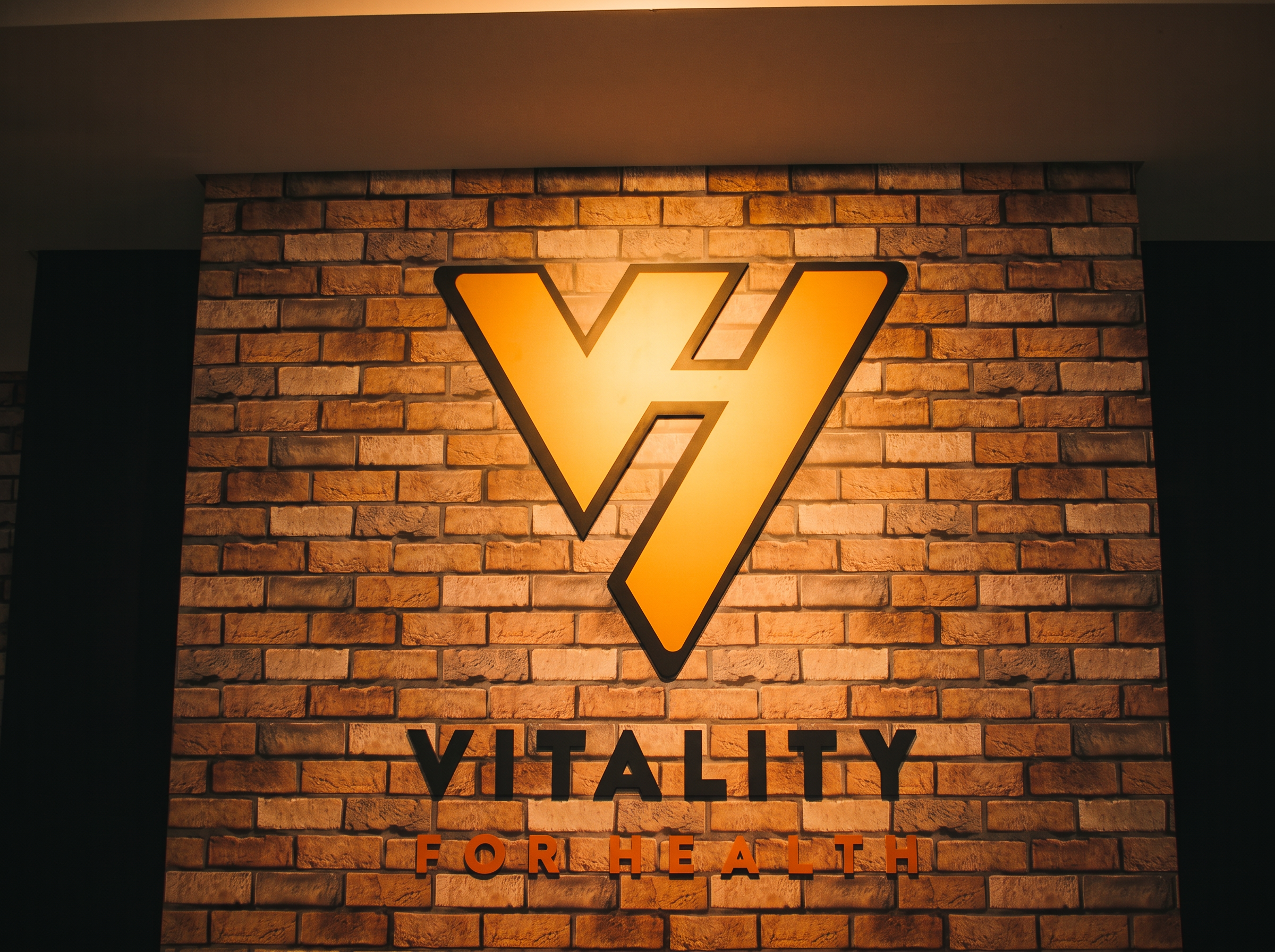 Parede de tijolos com a logo Vitality for Health em dourado iluminado